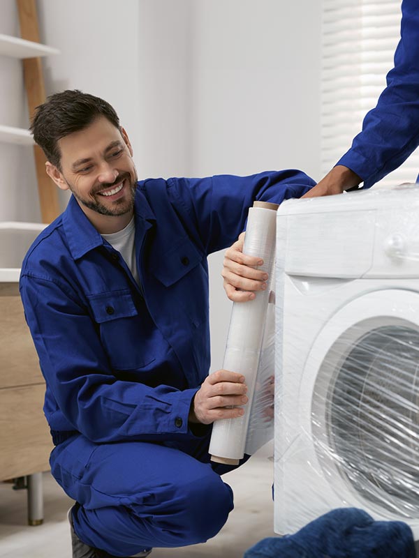 Professional mover applying protective stretch wrap to a washing machine as part of specialized appliance and other services