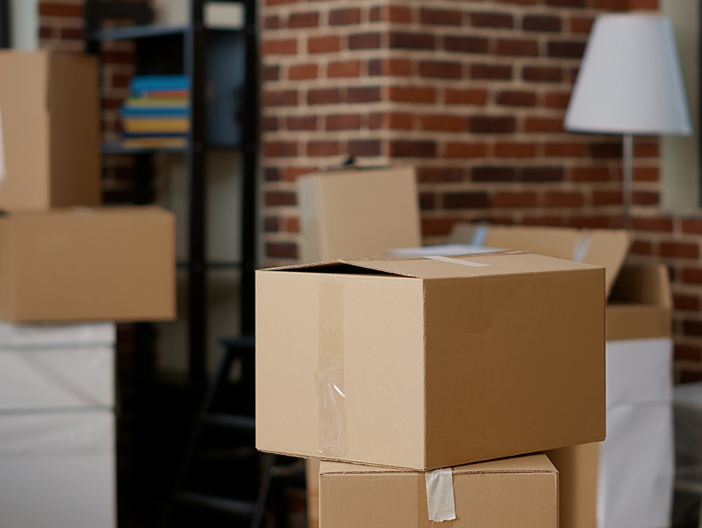 Cardboard moving boxes stacked in a room with brick walls for Smith & Sons Moving contact page